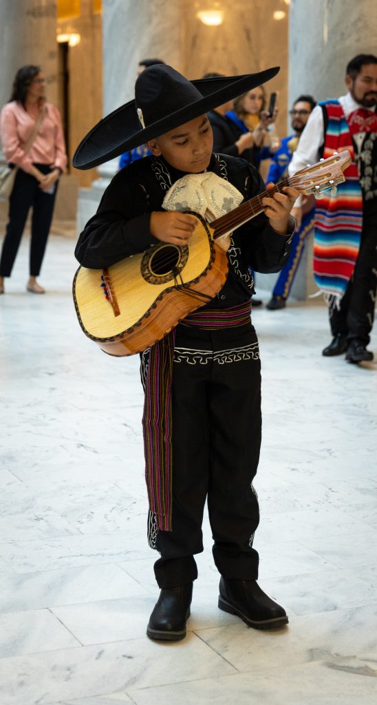 Young child wearing traje de charro playing the guitar.