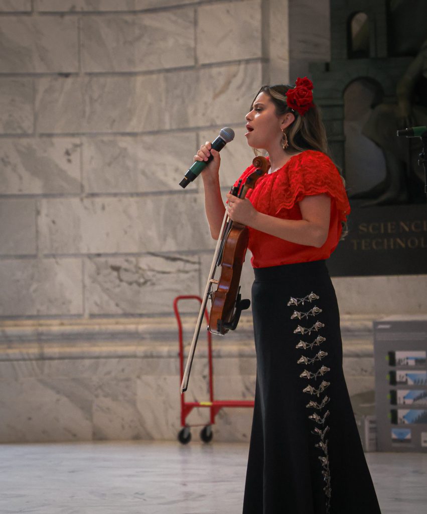 Woman holding a violin singing passionately into a microphone. 