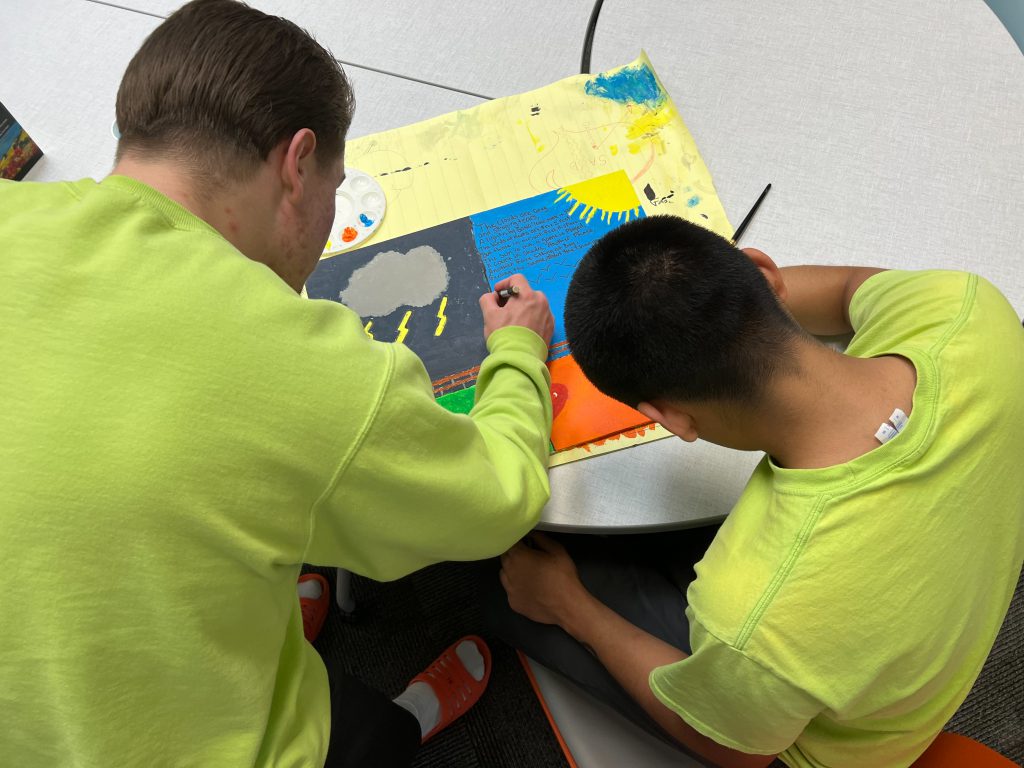 Close up image of two youth who are system involved working on a painting together. The picture is pictured below. 