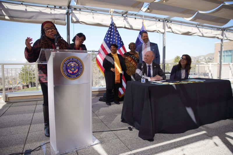 Betty Sawyer (Left Standing) speaking during a ceremony honoring the signing of Juneteenth National Freedom Day as an observed holiday in Utah with Governor Spencer Cox and Lieutenant Governor Diedre Henderson (seated) in Salt Lake City, April 18, 2021.