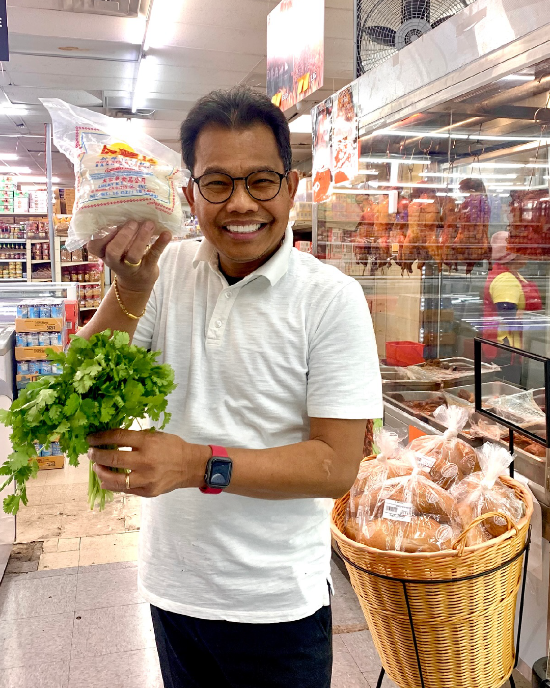 Man in a store holding a bag of rice and a bunch of cilantro, smiling at the camera.